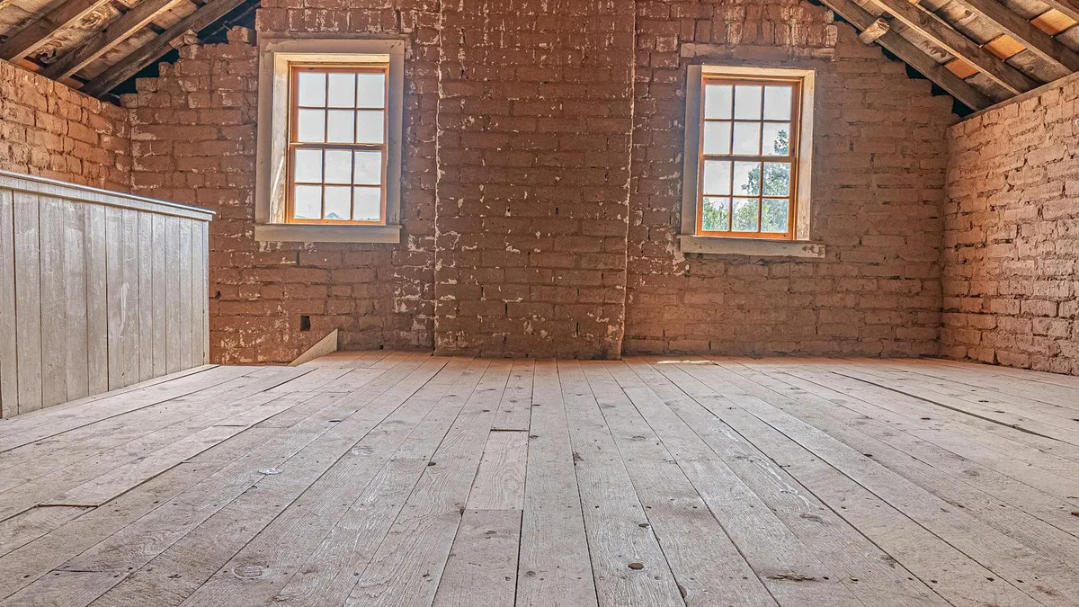 An empty residential attic with exposed wood-plank flooring and original roof framing.